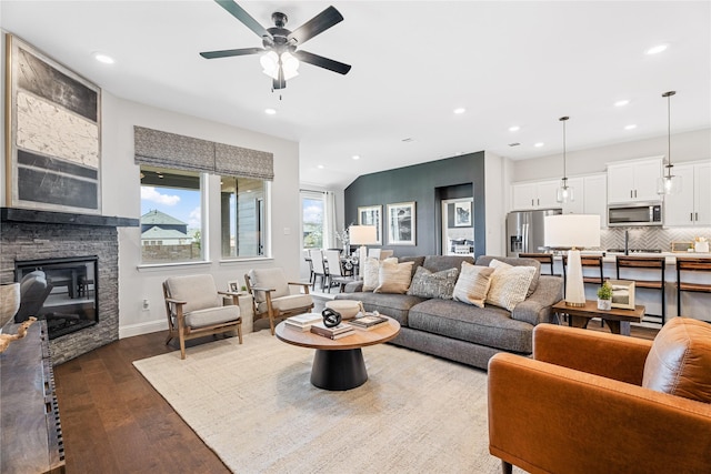 living room featuring dark wood-type flooring, ceiling fan, a stone fireplace, and sink