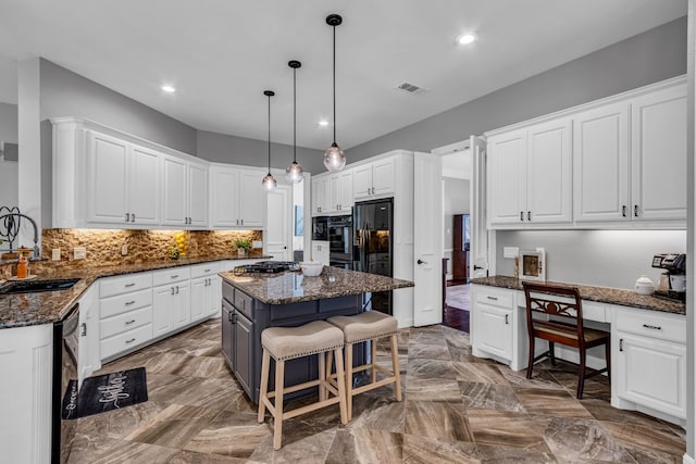 kitchen with sink, a kitchen island, white cabinets, dark stone countertops, and a breakfast bar area