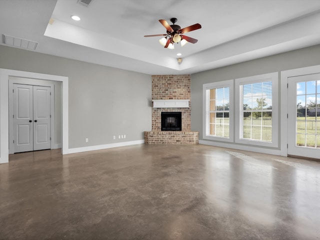 unfurnished living room with a raised ceiling, ceiling fan, and a brick fireplace