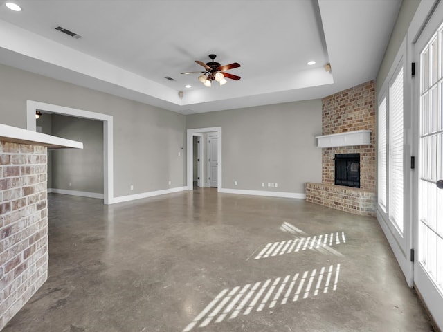 unfurnished living room featuring a raised ceiling, concrete floors, a brick fireplace, and a wealth of natural light