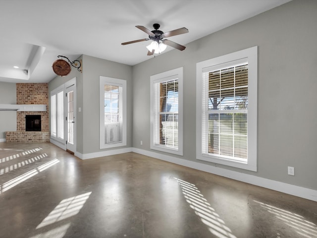 unfurnished living room with concrete flooring, a brick fireplace, and ceiling fan