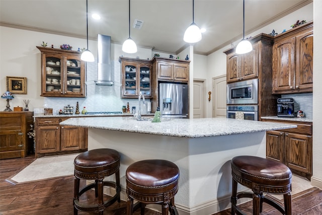 kitchen featuring appliances with stainless steel finishes, a center island, wall chimney exhaust hood, hardwood / wood-style flooring, and decorative backsplash