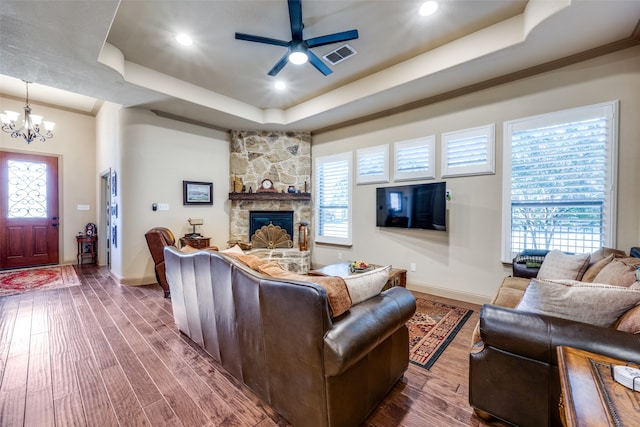 living room with a raised ceiling, a stone fireplace, wood-type flooring, and plenty of natural light