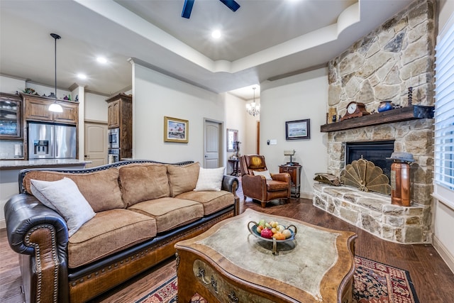 living room featuring dark hardwood / wood-style floors, ceiling fan with notable chandelier, a fireplace, and a raised ceiling