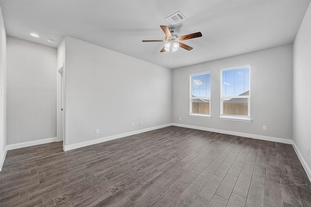 empty room with dark wood-style floors, visible vents, a ceiling fan, and baseboards