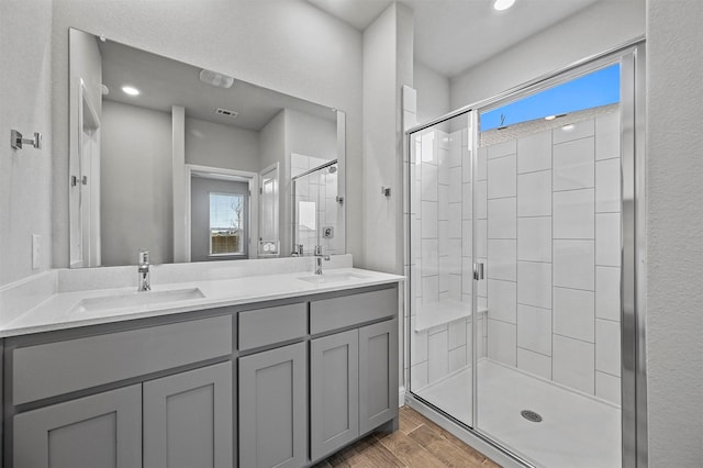 bathroom featuring double vanity, a sink, a shower stall, and wood finished floors