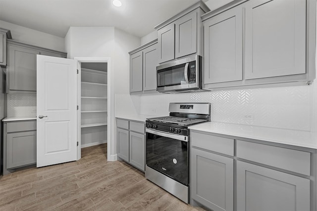 kitchen with gray cabinetry, stainless steel appliances, backsplash, and light wood-style flooring