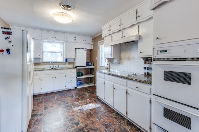 kitchen with sink, dark stone counters, white appliances, white cabinets, and decorative backsplash