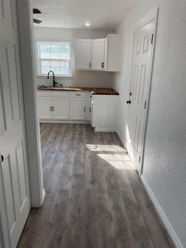 kitchen with light wood-type flooring, wood counters, sink, and white cabinets