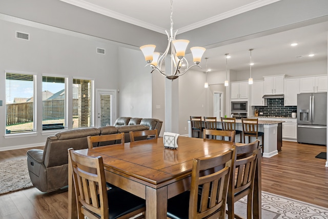 dining area with ornamental molding, wood-type flooring, and an inviting chandelier