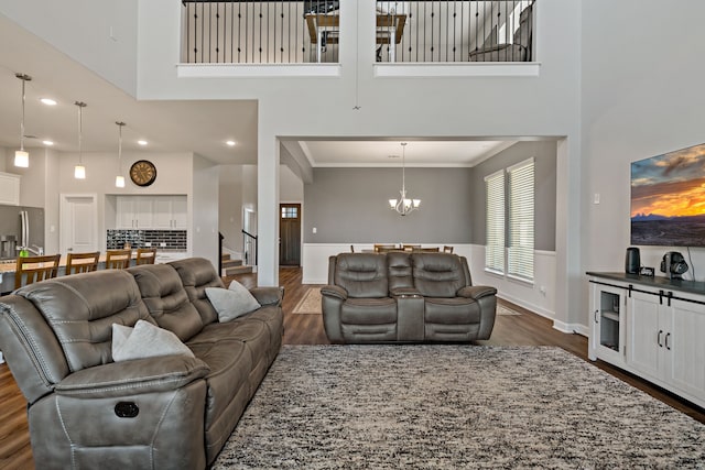 living room with a towering ceiling, an inviting chandelier, ornamental molding, and dark hardwood / wood-style flooring