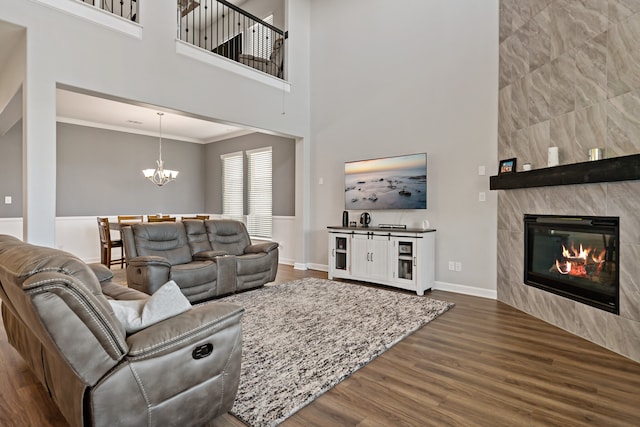 living room with dark wood-type flooring, a tiled fireplace, ornamental molding, and a high ceiling