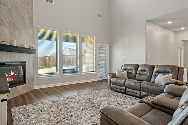 living room with a wealth of natural light, dark wood-type flooring, a towering ceiling, and a tile fireplace