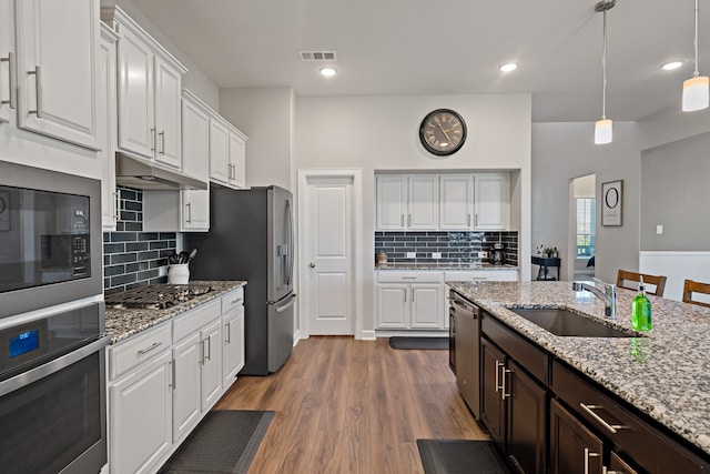 kitchen featuring wood-type flooring, light stone countertops, appliances with stainless steel finishes, sink, and white cabinets