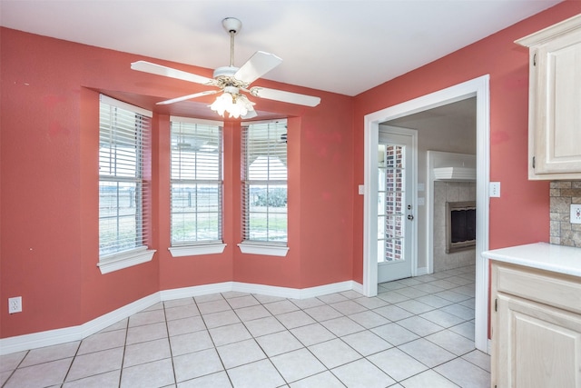 unfurnished dining area featuring a tiled fireplace, a wealth of natural light, ceiling fan, and light tile patterned floors