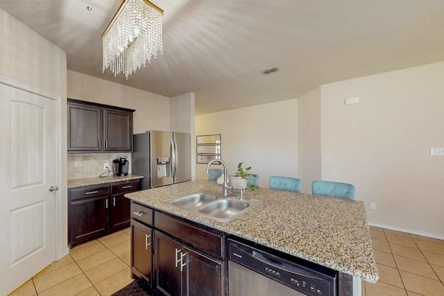 kitchen with appliances with stainless steel finishes, a kitchen island with sink, sink, light tile patterned floors, and a chandelier