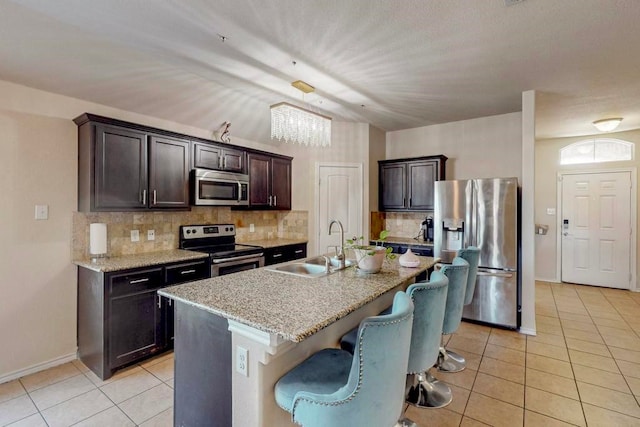 kitchen with sink, stainless steel appliances, an island with sink, decorative backsplash, and dark brown cabinets