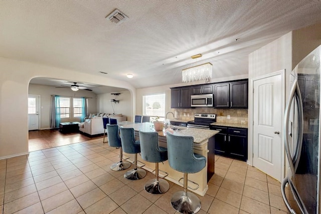 kitchen featuring ceiling fan, a kitchen breakfast bar, a center island with sink, light tile patterned floors, and appliances with stainless steel finishes