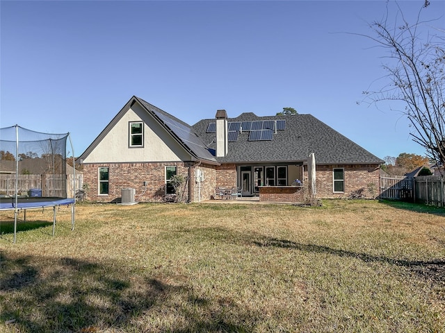 back of house featuring a lawn, a trampoline, a patio, and solar panels