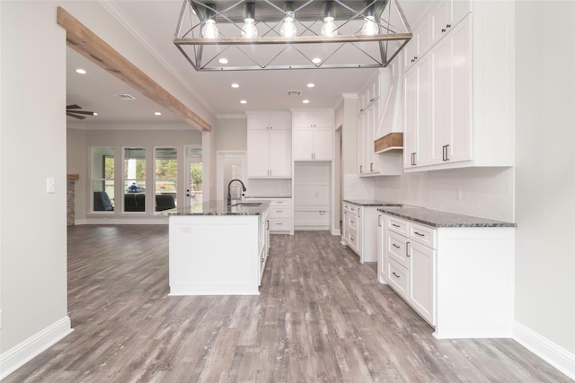 kitchen featuring ceiling fan, light wood-type flooring, an island with sink, and ornamental molding