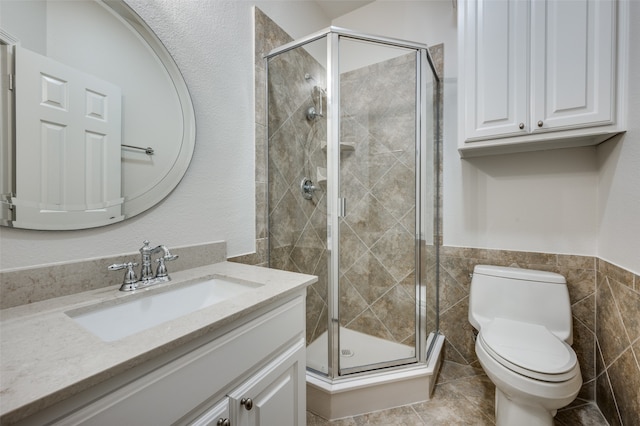 bathroom with toilet, a shower with door, tile walls, tile patterned flooring, and vanity