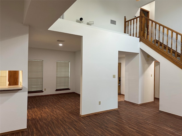 unfurnished living room featuring dark wood-type flooring and a towering ceiling