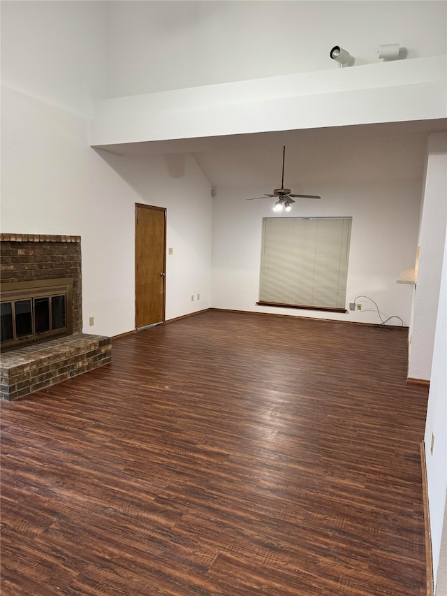 unfurnished living room featuring lofted ceiling, ceiling fan, dark wood-type flooring, and a brick fireplace