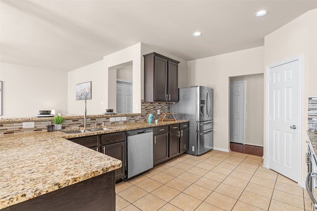 kitchen with appliances with stainless steel finishes, sink, backsplash, dark brown cabinetry, and light stone counters