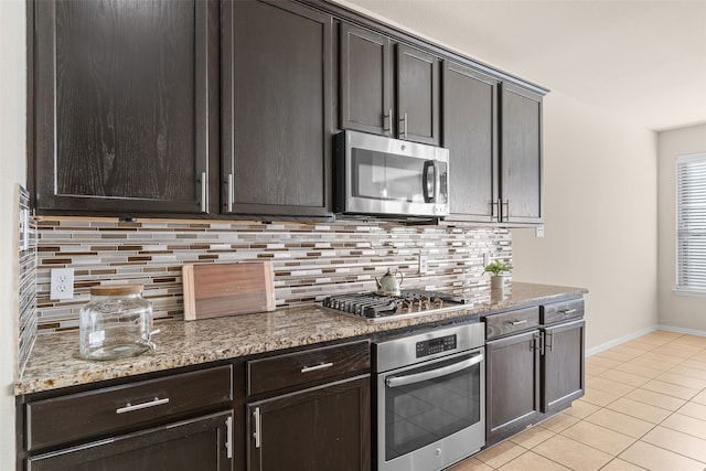 kitchen featuring decorative backsplash, dark brown cabinets, dark stone countertops, light tile patterned flooring, and appliances with stainless steel finishes