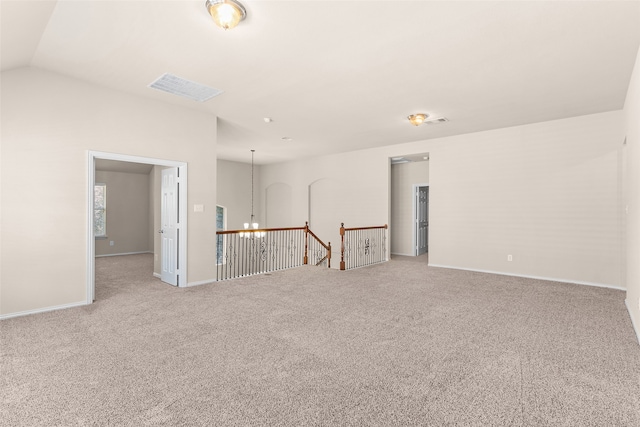 carpeted spare room with an inviting chandelier and vaulted ceiling