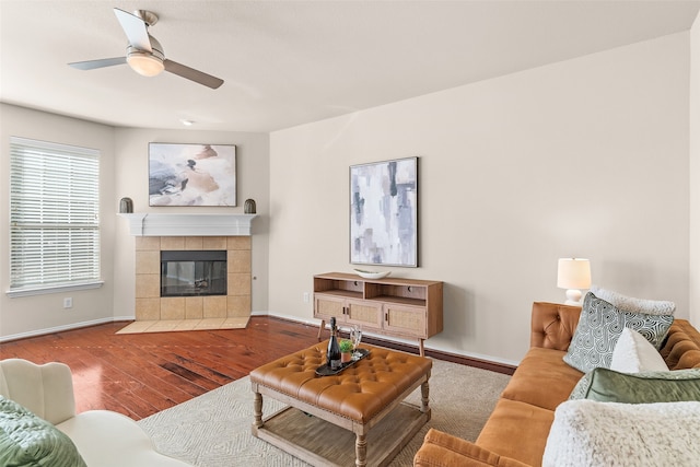 living room featuring hardwood / wood-style flooring, a tiled fireplace, and ceiling fan