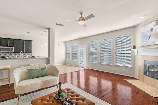 living room featuring ceiling fan, wood-type flooring, sink, and a tile fireplace