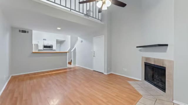 unfurnished living room featuring a high ceiling, light tile patterned floors, ceiling fan, and a tiled fireplace