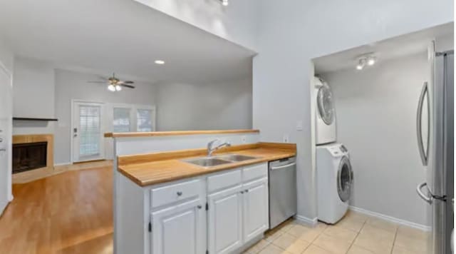 kitchen with appliances with stainless steel finishes, ceiling fan, sink, white cabinets, and stacked washer / drying machine