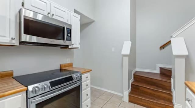 kitchen with butcher block countertops, white cabinetry, light tile patterned floors, and appliances with stainless steel finishes