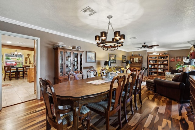 dining space featuring light wood finished floors, a textured ceiling, ceiling fan with notable chandelier, visible vents, and ornamental molding