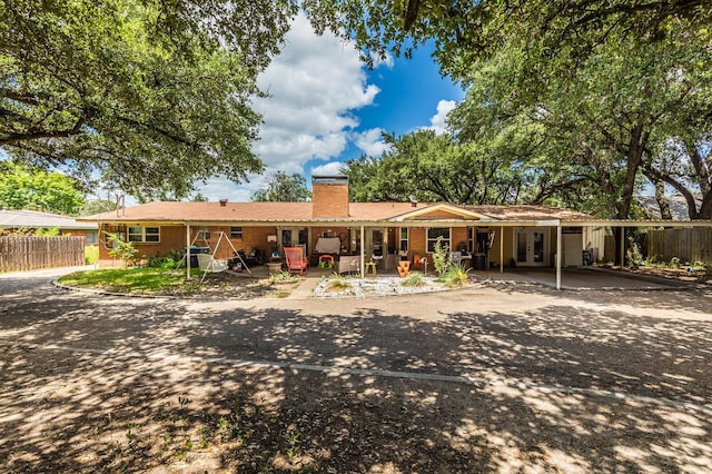 back of house with fence, french doors, an attached carport, a chimney, and brick siding