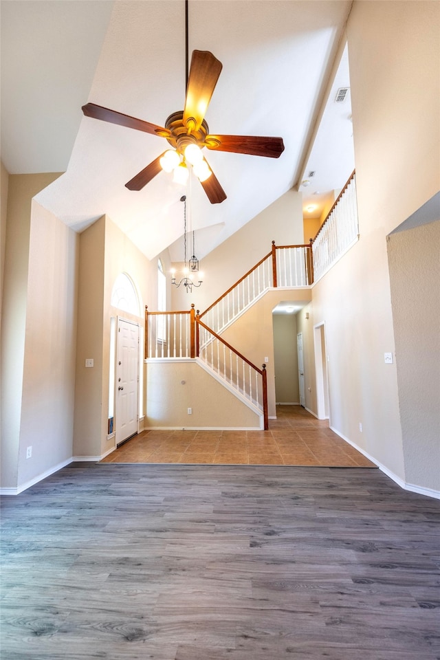 unfurnished living room featuring high vaulted ceiling, wood-type flooring, and ceiling fan with notable chandelier