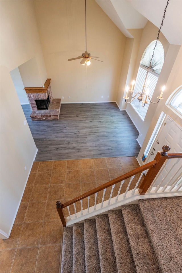 interior space featuring hardwood / wood-style flooring, high vaulted ceiling, ceiling fan with notable chandelier, and a brick fireplace