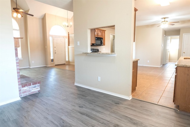 kitchen with light stone counters, ceiling fan with notable chandelier, and light wood-type flooring