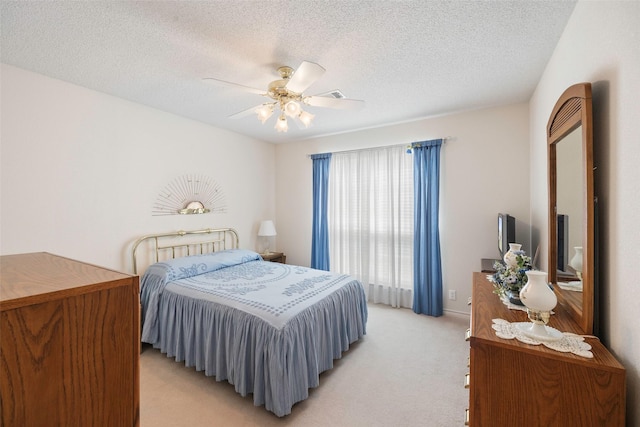 bedroom with ceiling fan, light colored carpet, and a textured ceiling