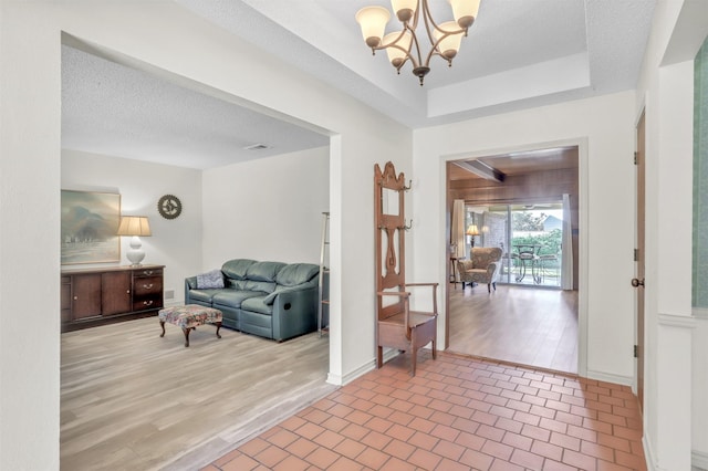 foyer entrance featuring wood-type flooring, a notable chandelier, a textured ceiling, and a tray ceiling