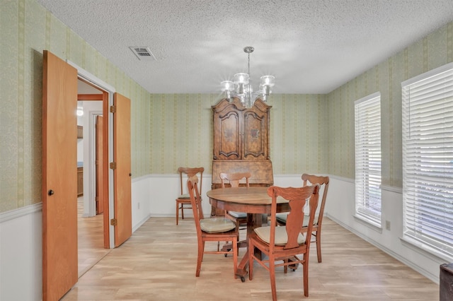 dining space featuring a textured ceiling, an inviting chandelier, and light hardwood / wood-style floors