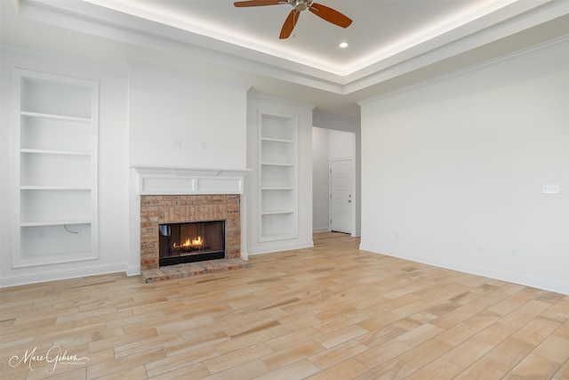 unfurnished living room featuring a brick fireplace, built in shelves, light hardwood / wood-style floors, and ceiling fan