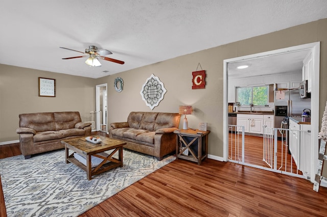 living room featuring sink, hardwood / wood-style floors, a textured ceiling, and ceiling fan