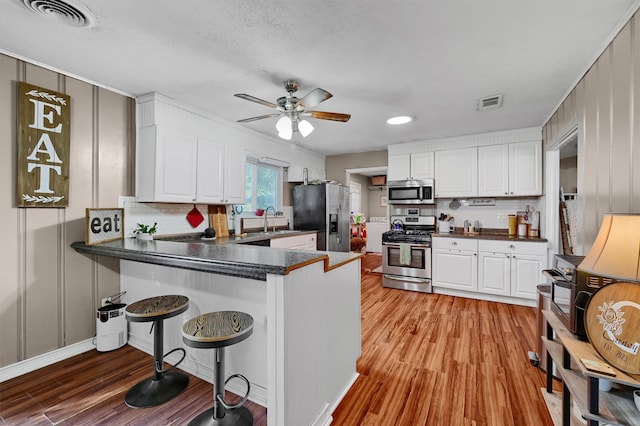 kitchen featuring appliances with stainless steel finishes, kitchen peninsula, light hardwood / wood-style flooring, and white cabinets