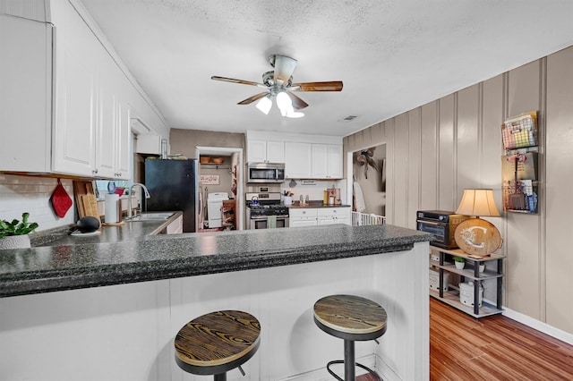 kitchen with appliances with stainless steel finishes, kitchen peninsula, light wood-type flooring, and white cabinets