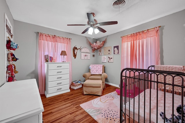 bedroom with light hardwood / wood-style floors, multiple windows, a crib, and ceiling fan