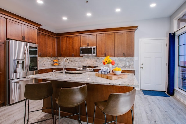 kitchen with a breakfast bar area, a center island with sink, stainless steel appliances, and light hardwood / wood-style floors