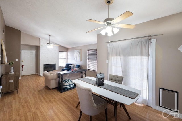 dining room with ceiling fan, light hardwood / wood-style flooring, lofted ceiling, and a fireplace